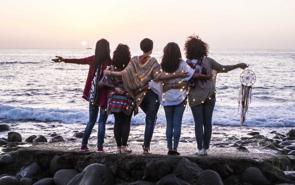Love and friendship concept with group of female people enjoying the sunset on the ocean together -