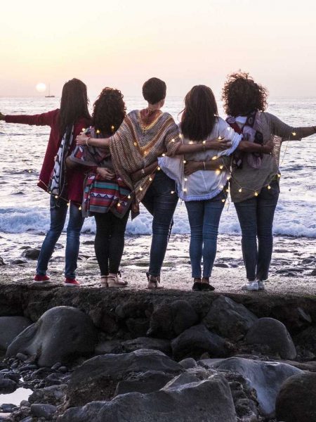 Love and friendship concept with group of female people enjoying the sunset on the ocean together -